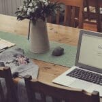 Macbook open to Google search on wooden table with iPhone & newspaper nearby